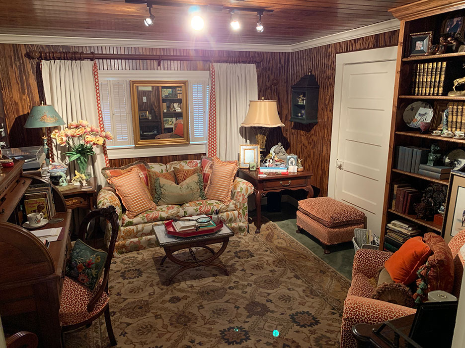 Cozy living room with patterned sofa, lamps, wood trim, and a shelf-lined wall
