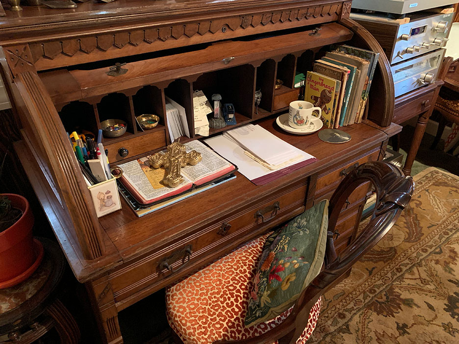 Antique wooden sideboard with teacups, books, papers, and a patterned cloth draped over the front.