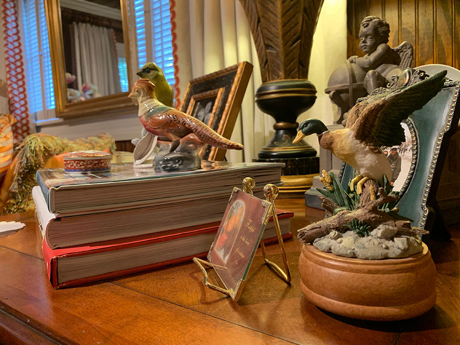 Decorative tabletop display with a bird figurine on books, a plant, and a small sculpture on a wooden surface