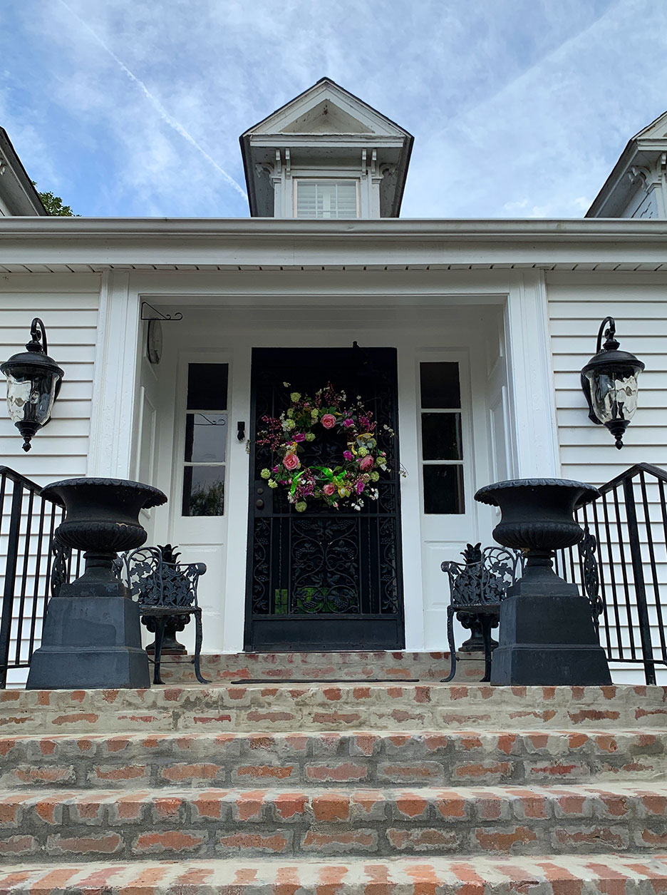 White house front porch with black railings, brick steps, and a floral wreath on the front door