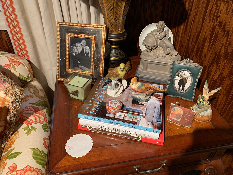 Wooden nightstand with framed photos, books, a small figurine, and decorative items beside a patterned curtain.