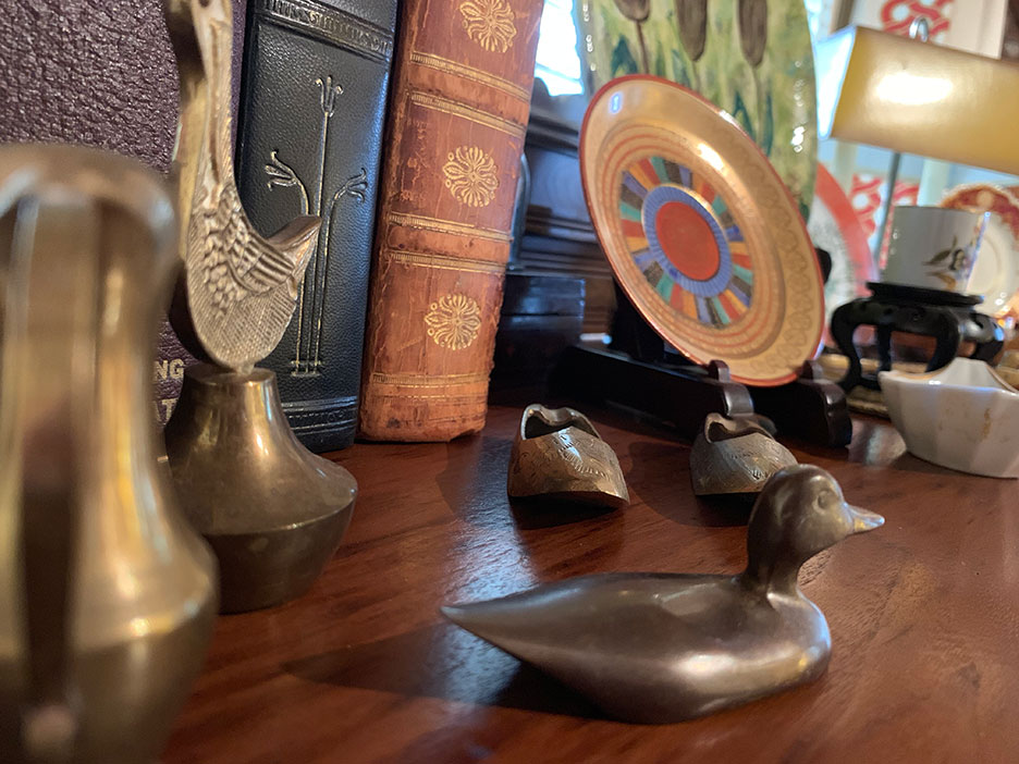 Decorative metal figurines on a wooden table with books and a colorful round ornament in the background