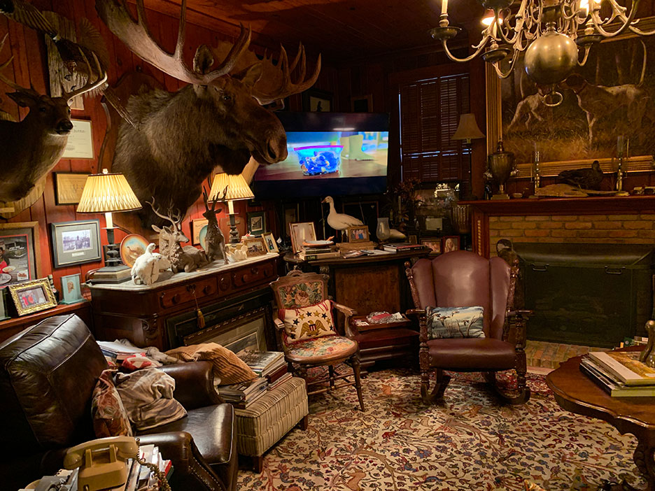 Cozy wood-paneled study with mounted moose, leather chairs, fireplace, and patterned rug