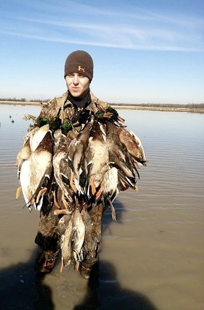 Person standing in shallow water wearing a large pile of dead birds and a brown beanie