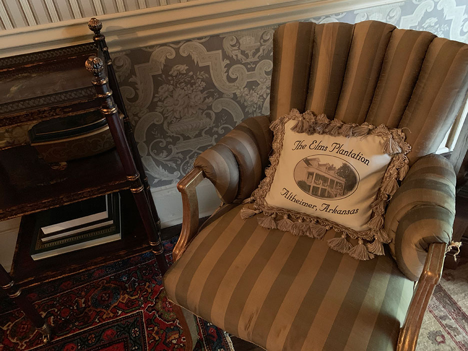 Striped armchair with decorative pillow beside a dark wood table and patterned wallpaper