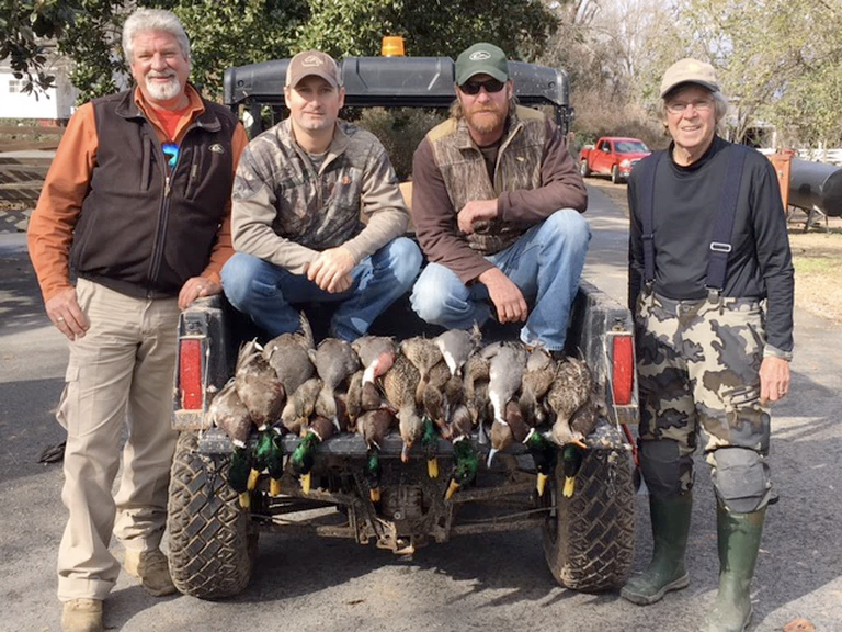 Four hunters pose with a row of ducks on the back of an off-road vehicle.