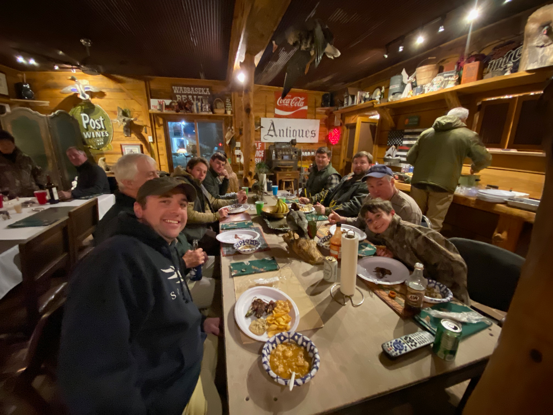 People seated at a rustic restaurant table, smiling and eating inside a warm wooden dining room.