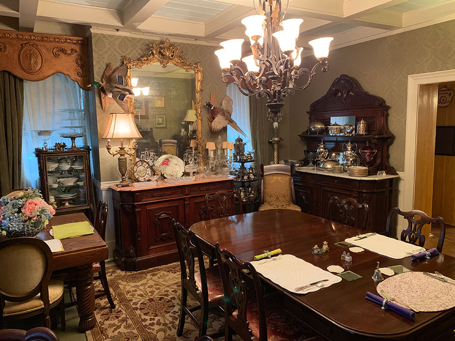 Elegant dining room with dark wood furniture, chandelier, ornate mirror, and set table