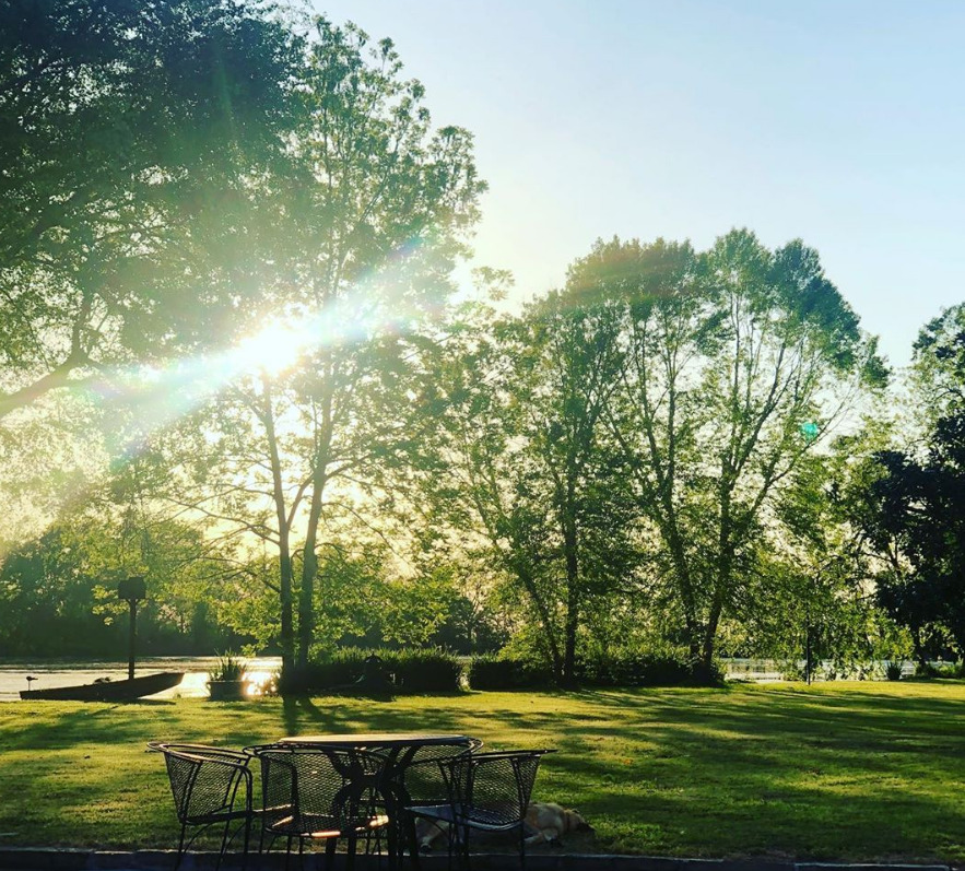 Sunlit park with trees, green lawn, and patio table and chairs under bright morning light