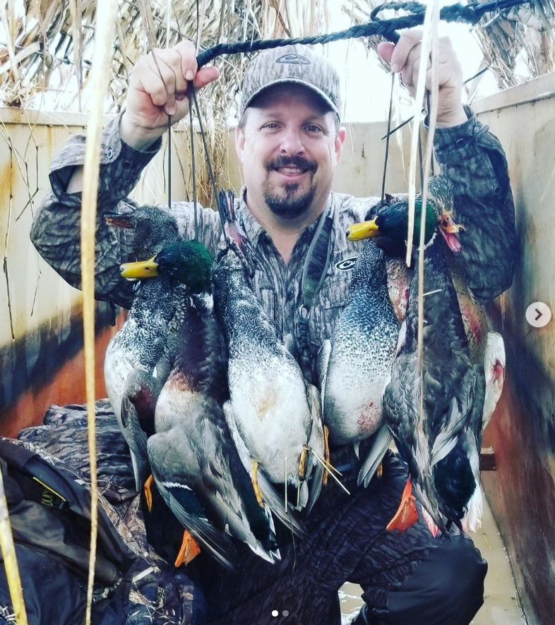 Hunter holding several dead ducks by their strings in an outdoor blind