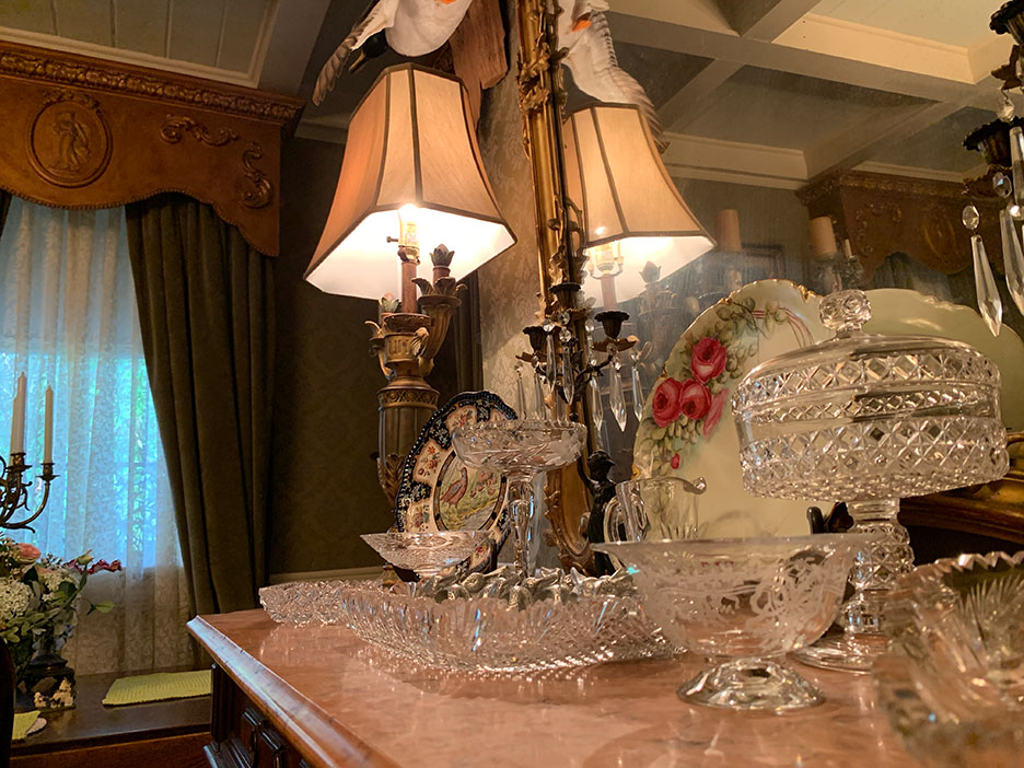 Crystal dining table with ornate lamp, glass dishes, and floral arrangement in a warmly lit room