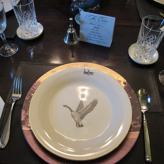 Elegant dining table setting with white plate, bird design, silverware, crystal glasses, and menu card