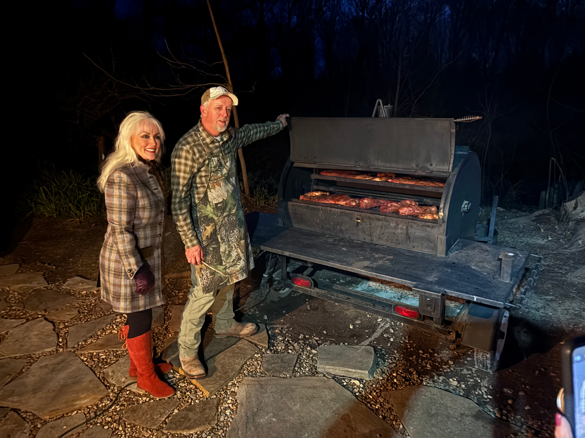 Two people standing by an open fire pit at night, one holding a roasting stick.