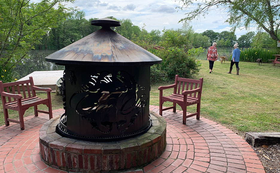Brick fire pit with metal cover and benches in a park, with two people in the background