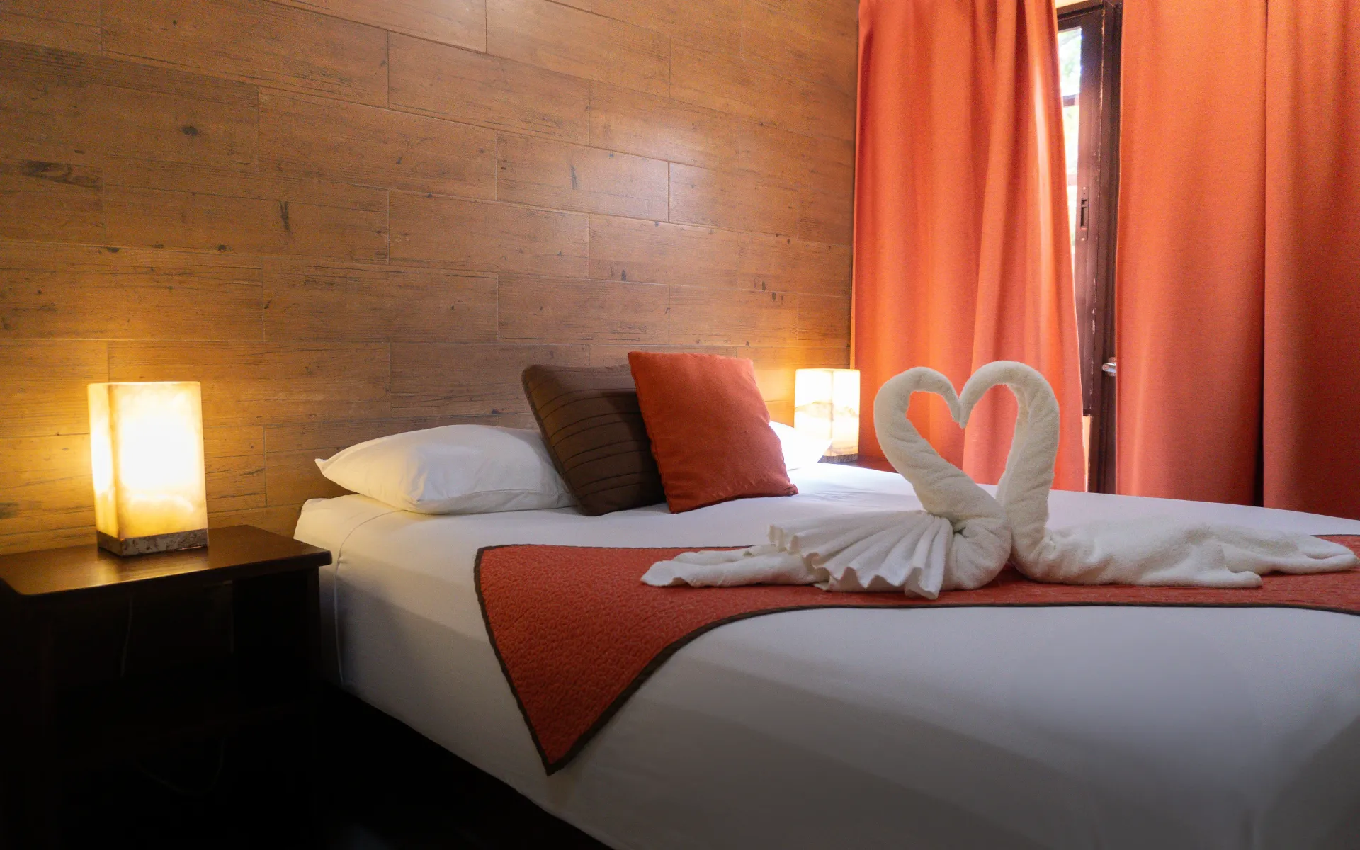 Una acogedora cama de hotel con sábanas blancas, almohadas naranjas, toallas dobladas..