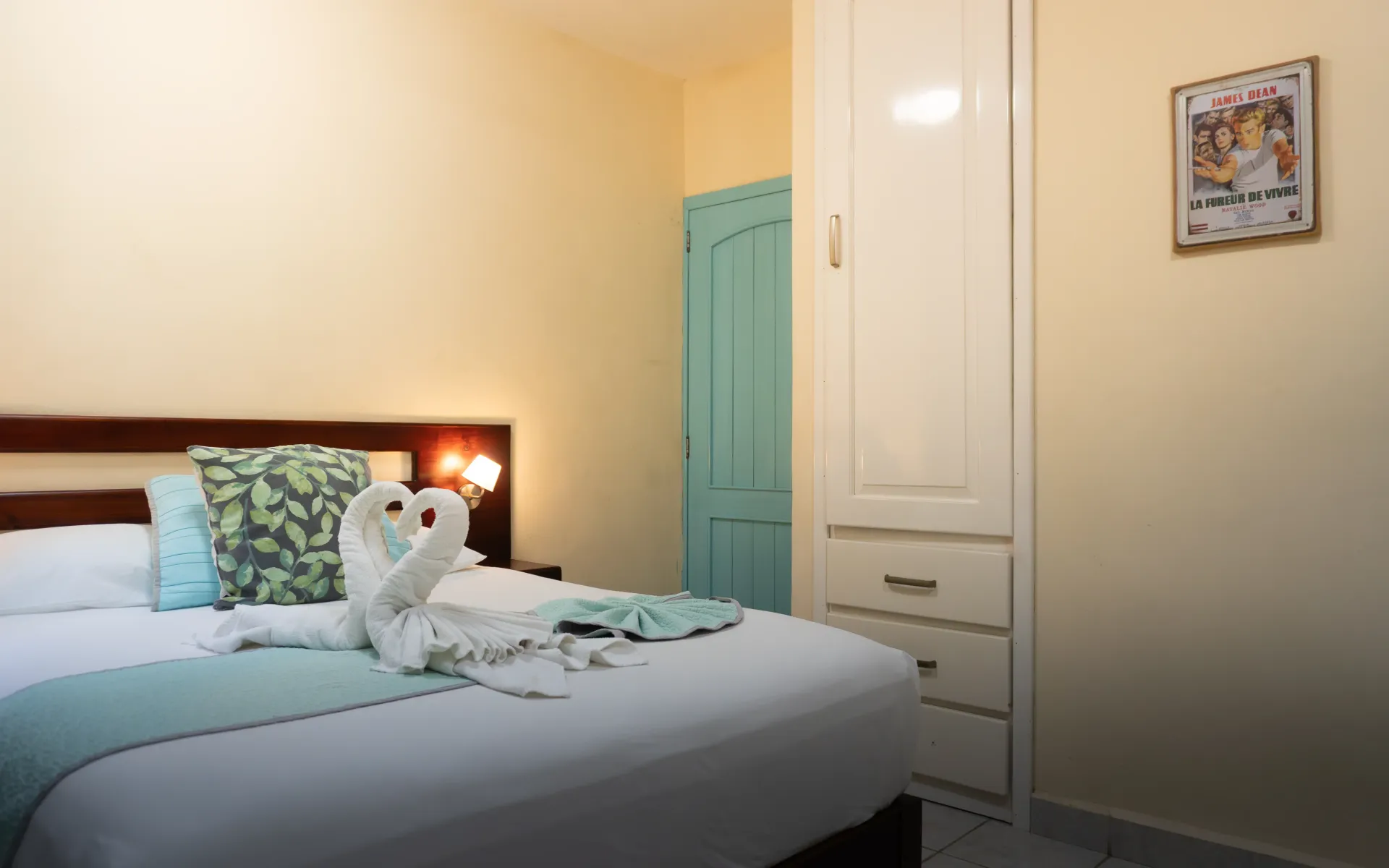 Una cama bien hecha con animales de peluche en un dormitorio acogedor, junto a un armario y cuadros en la pared.