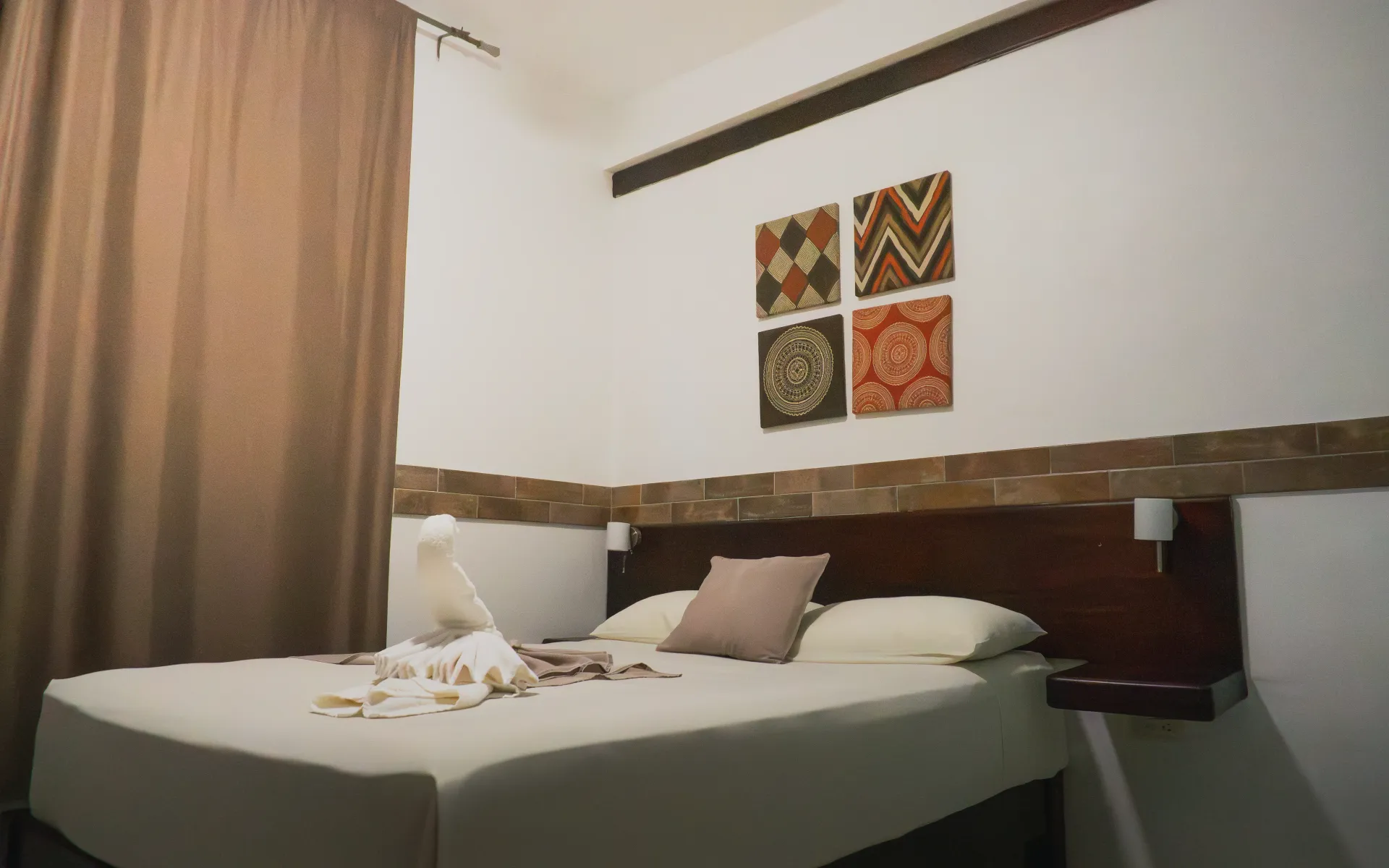 Dormitorio con una cama bien hecha, cortinas marrones y un cuadro en la pared sobre el cabecero.