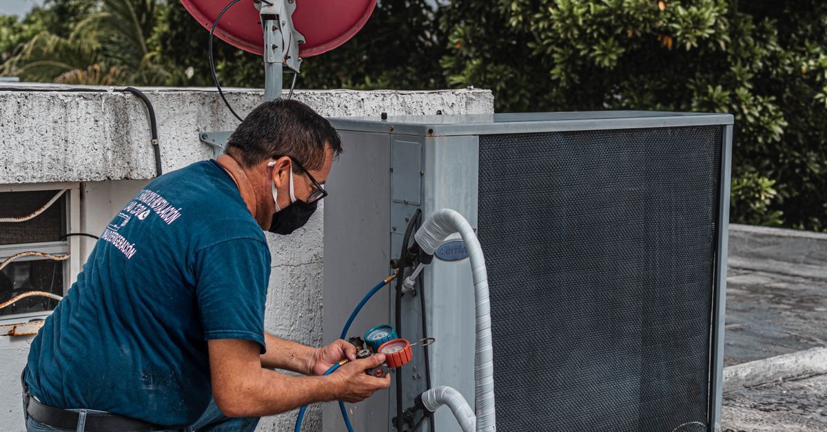Técnico inspeccionando una unidad de climatización exterior con un manómetro y una manguera.