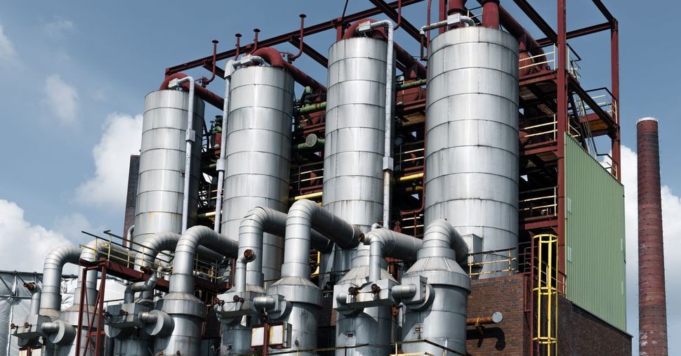 Planta industrial con tanques plateados, grandes tuberías y estructura de acero contra un cielo azul.