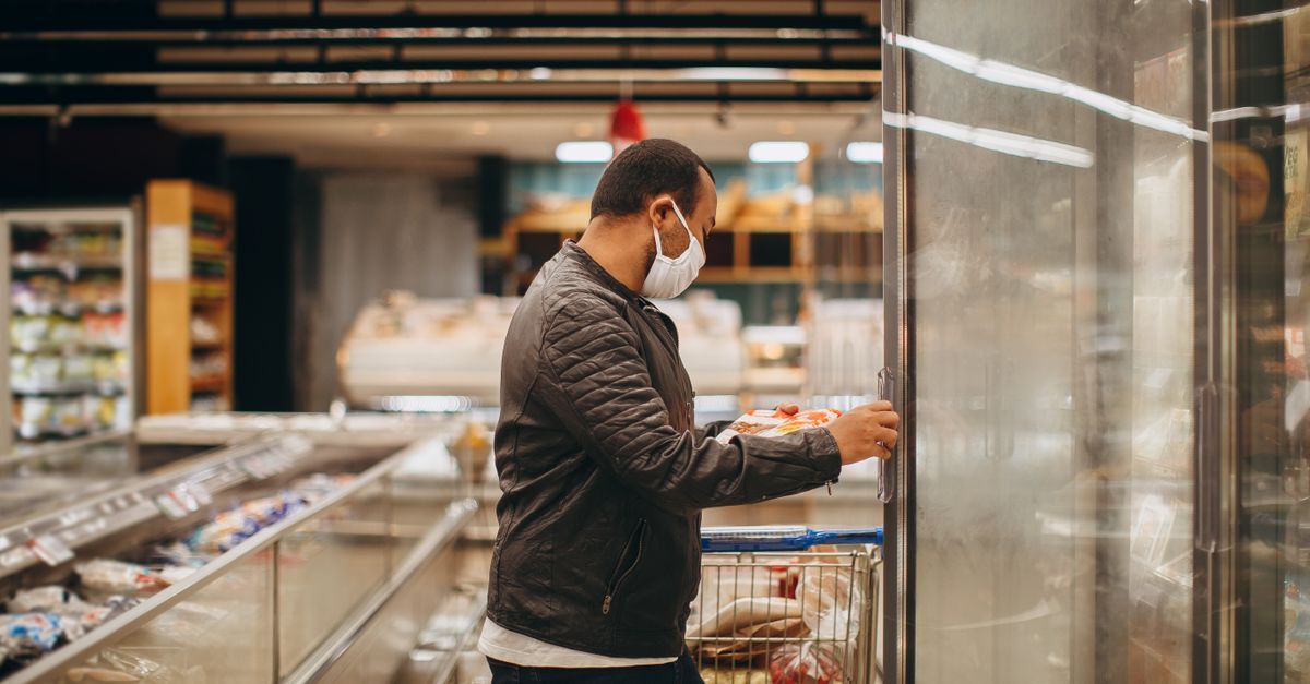 Un comprador enmascarado mete la mano en un pasillo de productos refrigerados dentro de un supermercado.