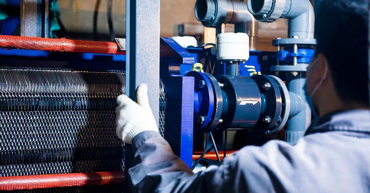 Técnico inspeccionando tuberías y válvulas industriales azules en una sala de máquinas.