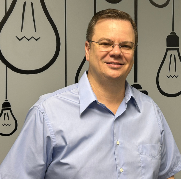 A man wearing glasses and a black shirt is smiling for the camera.