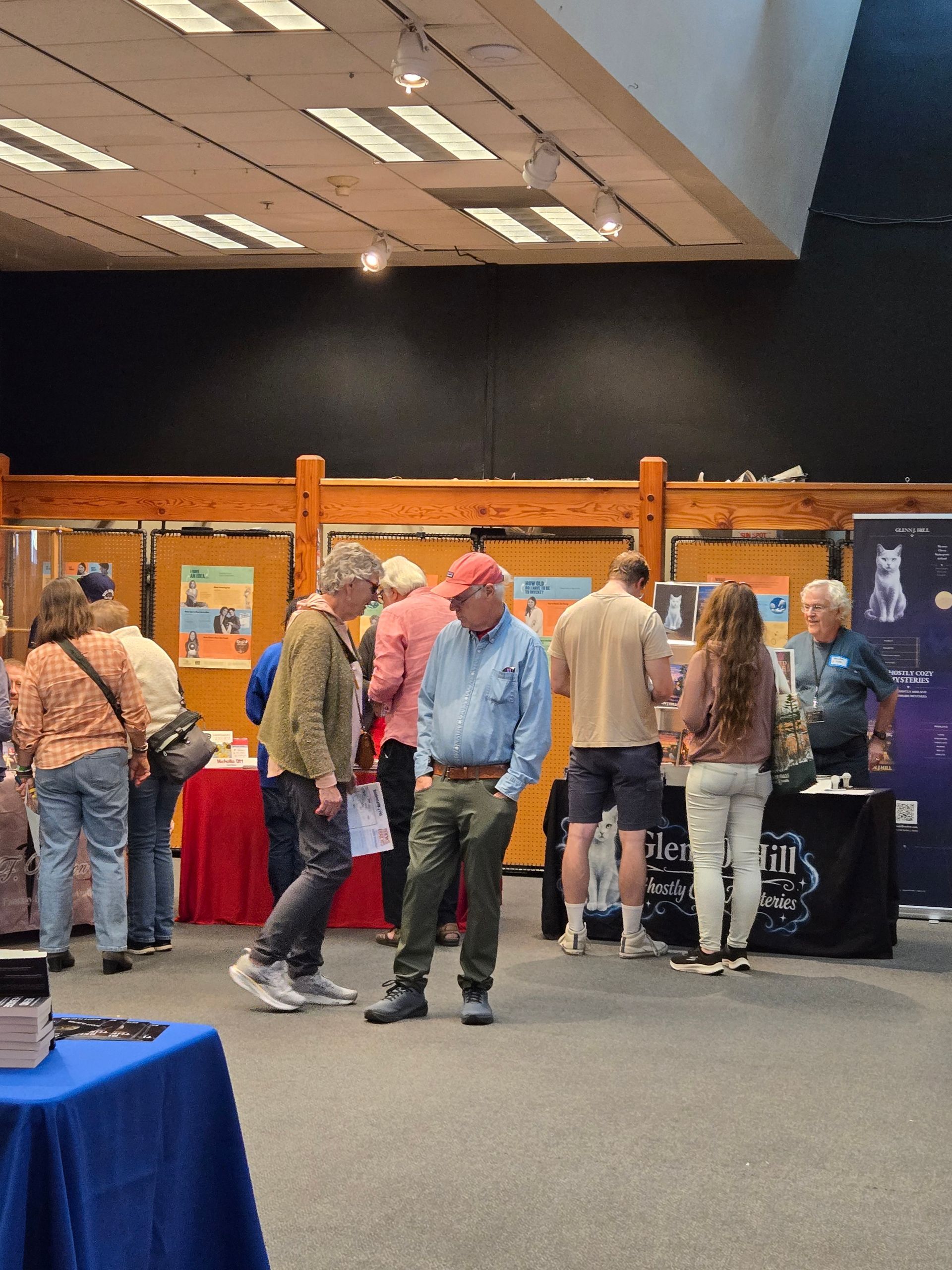 People browsing tables at an indoor event booth area with red tablecloths.