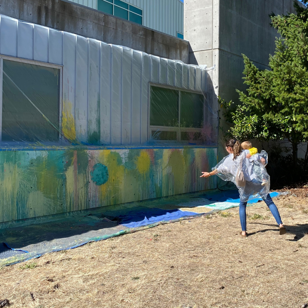 a woman holding a small child throws a paint balloon at a scienceworks wall
