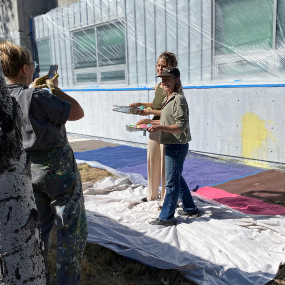 People painting a wall outdoors on drop cloths, with trays of paint balloons.