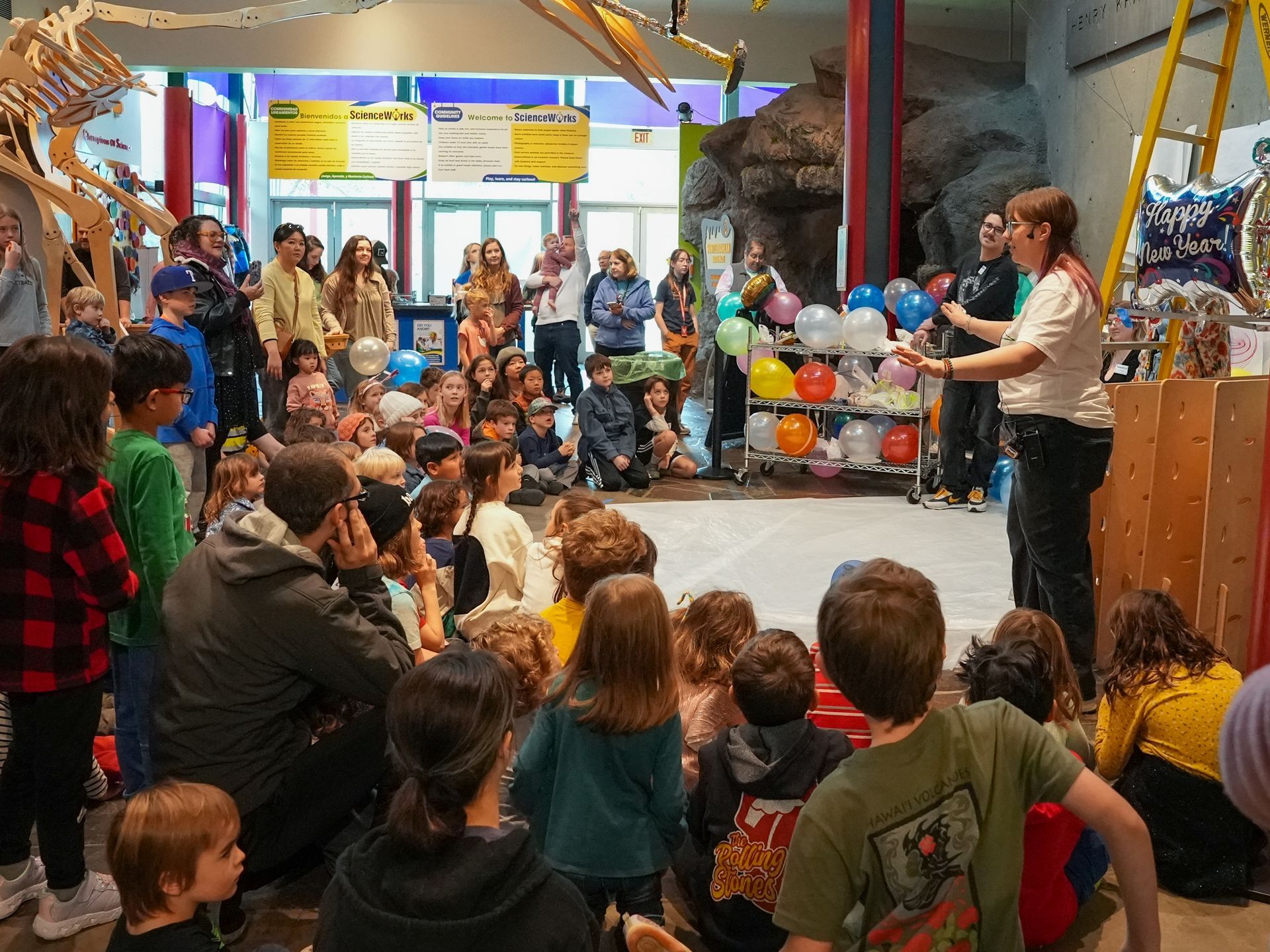 Group of children listening to the egg drop challenge facilitator  at ScienceWorks, surrounded by colorful decorations and exhibits.