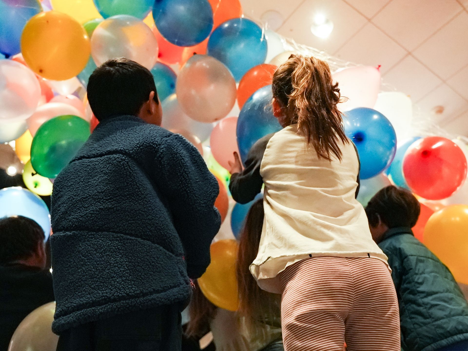 Children reaching toward colorful balloons falling from the ceiling in a bright indoor room