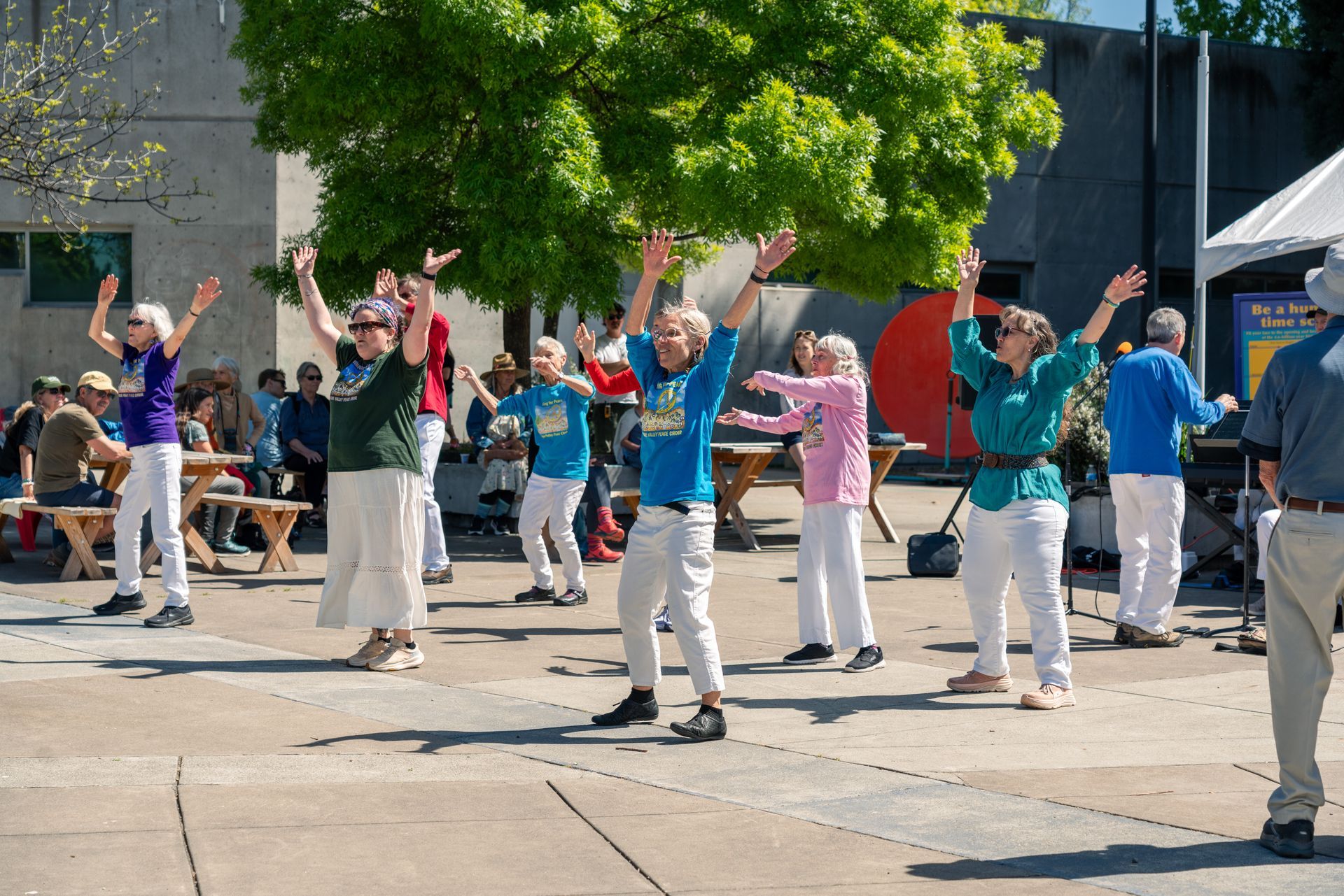 People dancing outdoors in a group, raising their arms on a sunny scienceworks plaza