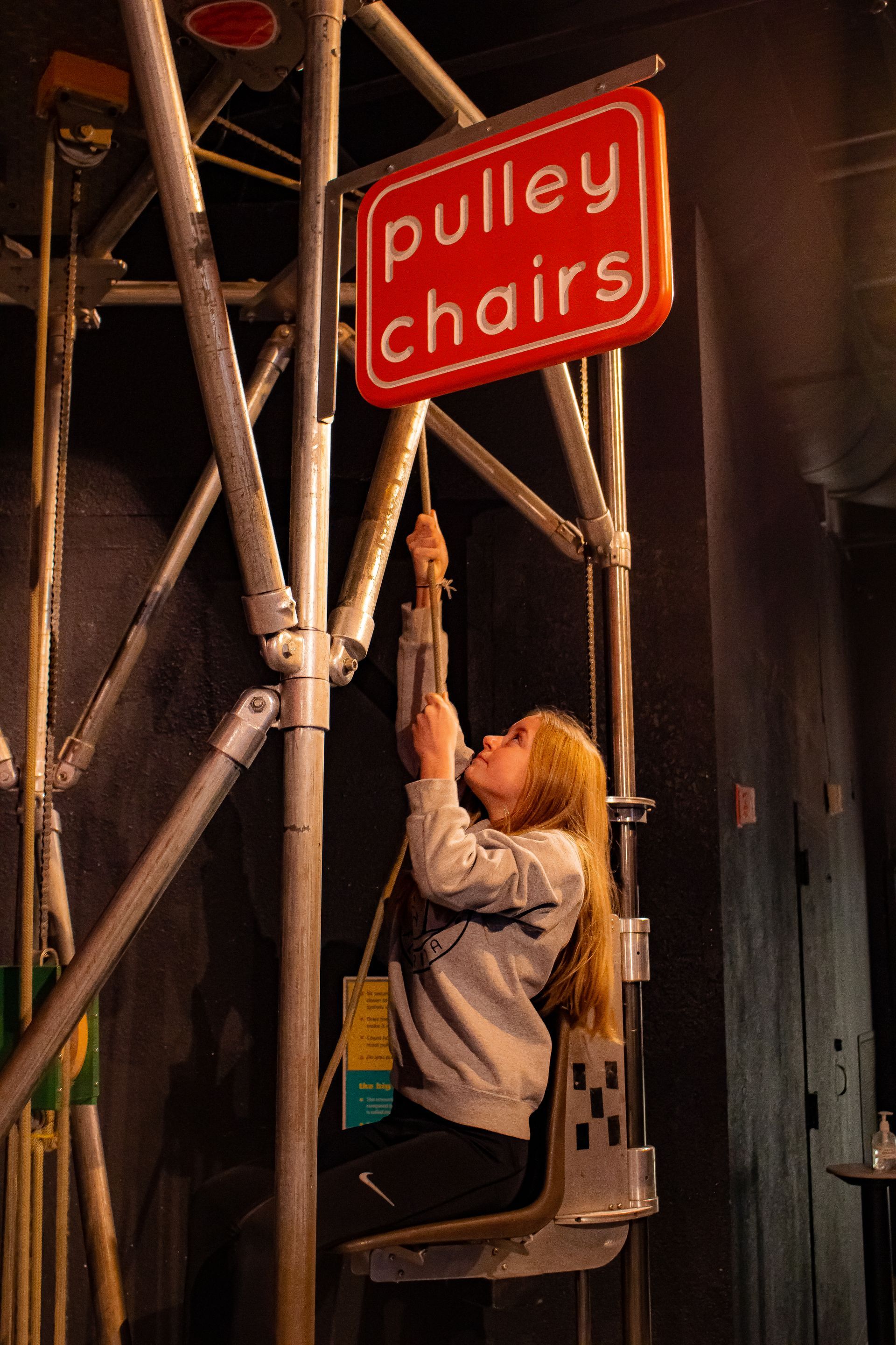 A girl pulls herself up on the Pulley Chairs, an exhibit at ScienceWorks Museum in Ashland