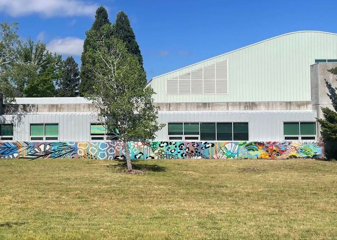 ScienceWorks building with colorful mural, large tree, and grassy field under a blue sky