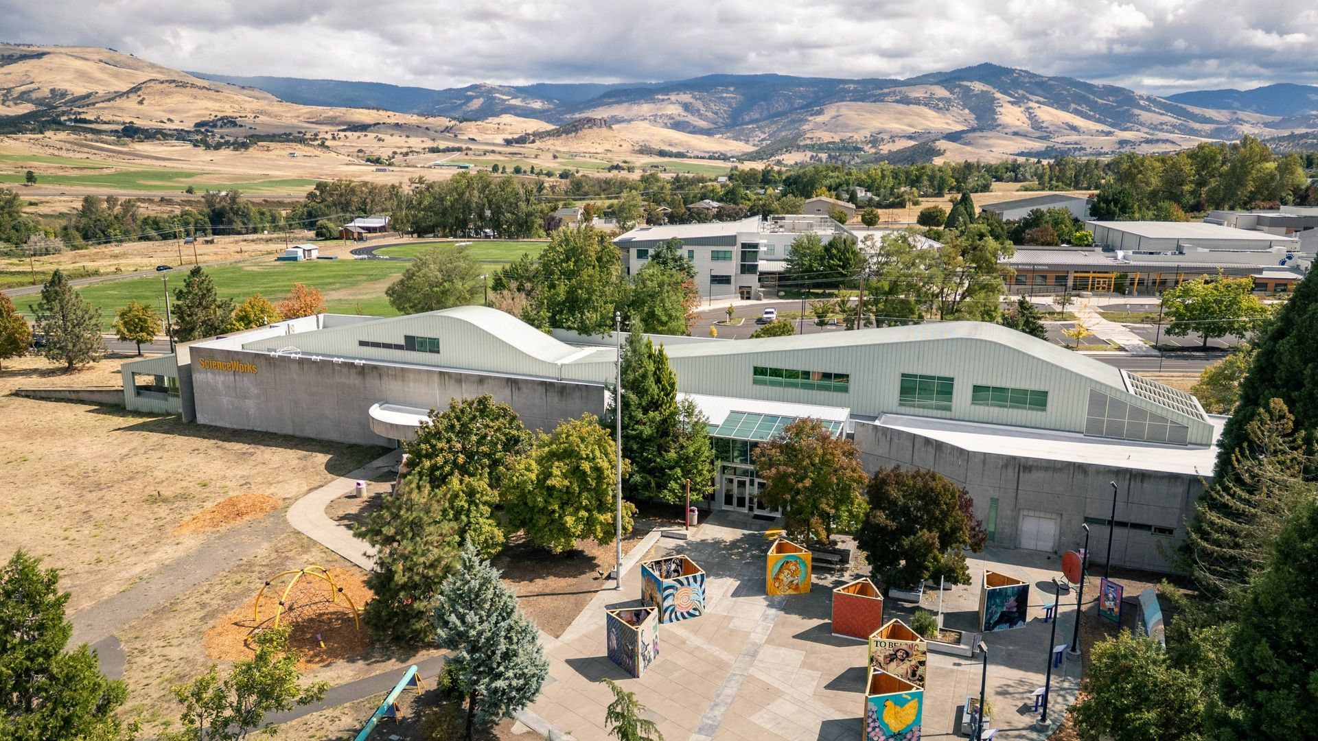 Aerial view of the ScienceWorks building with playground, trees, and mountains in the background