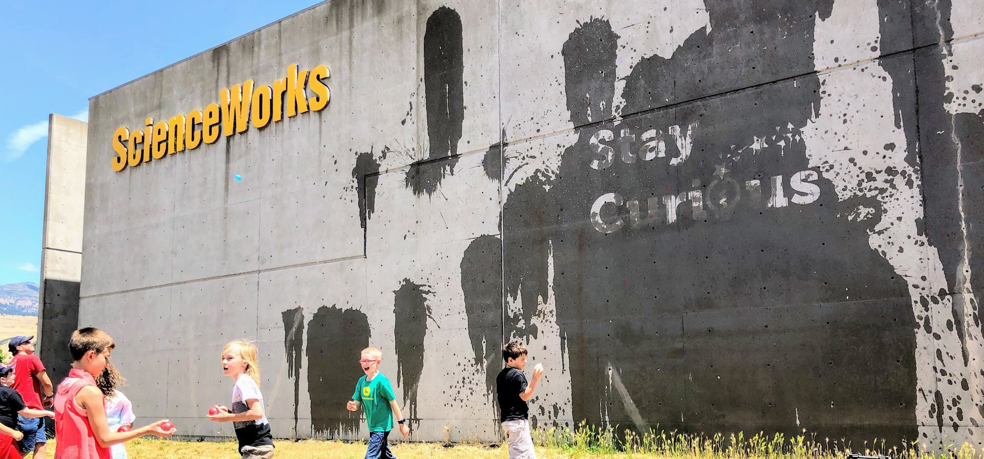 On the outside wall of the ScienceWorks building, children are throwing water balloons to reveal the message