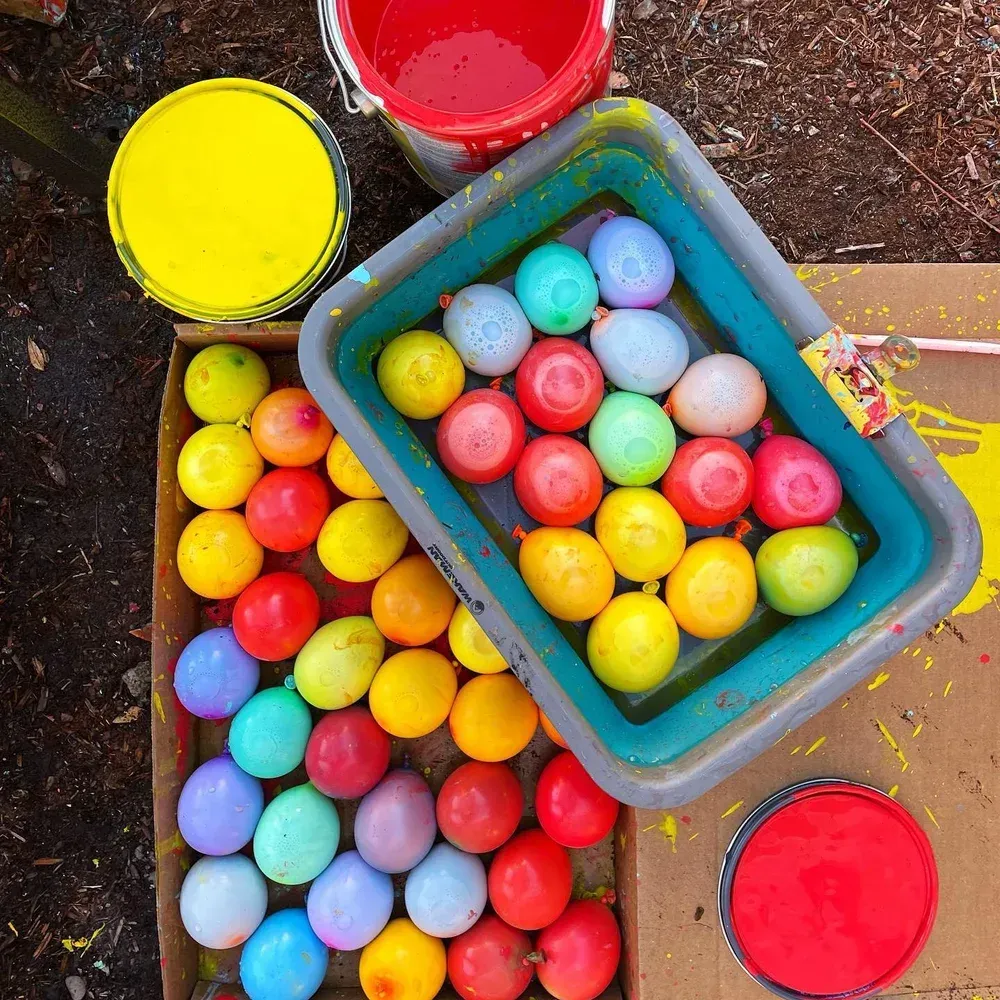 Colorful paint-covered balloons in tubs and trays on a work surface, overhead view