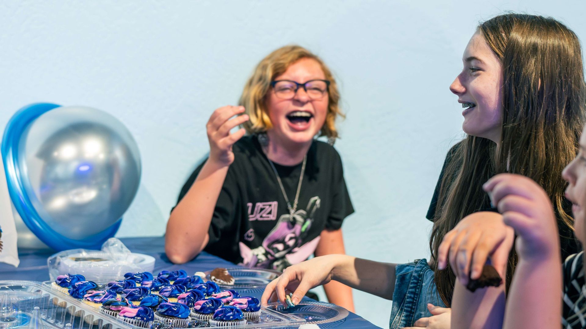 Two girls laughing and eating cupcakes at a birthday party in the celebration room at ScienceWorks