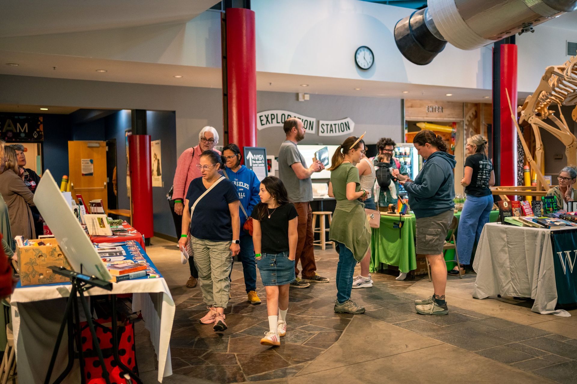 People browsing colorful booths at an indoor fair or market under bright lights