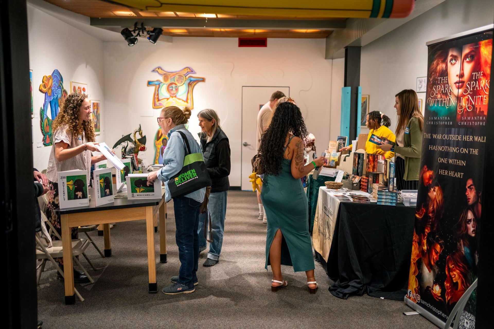 Indoor room with paintings, posters, and visitors browsing at a book fair