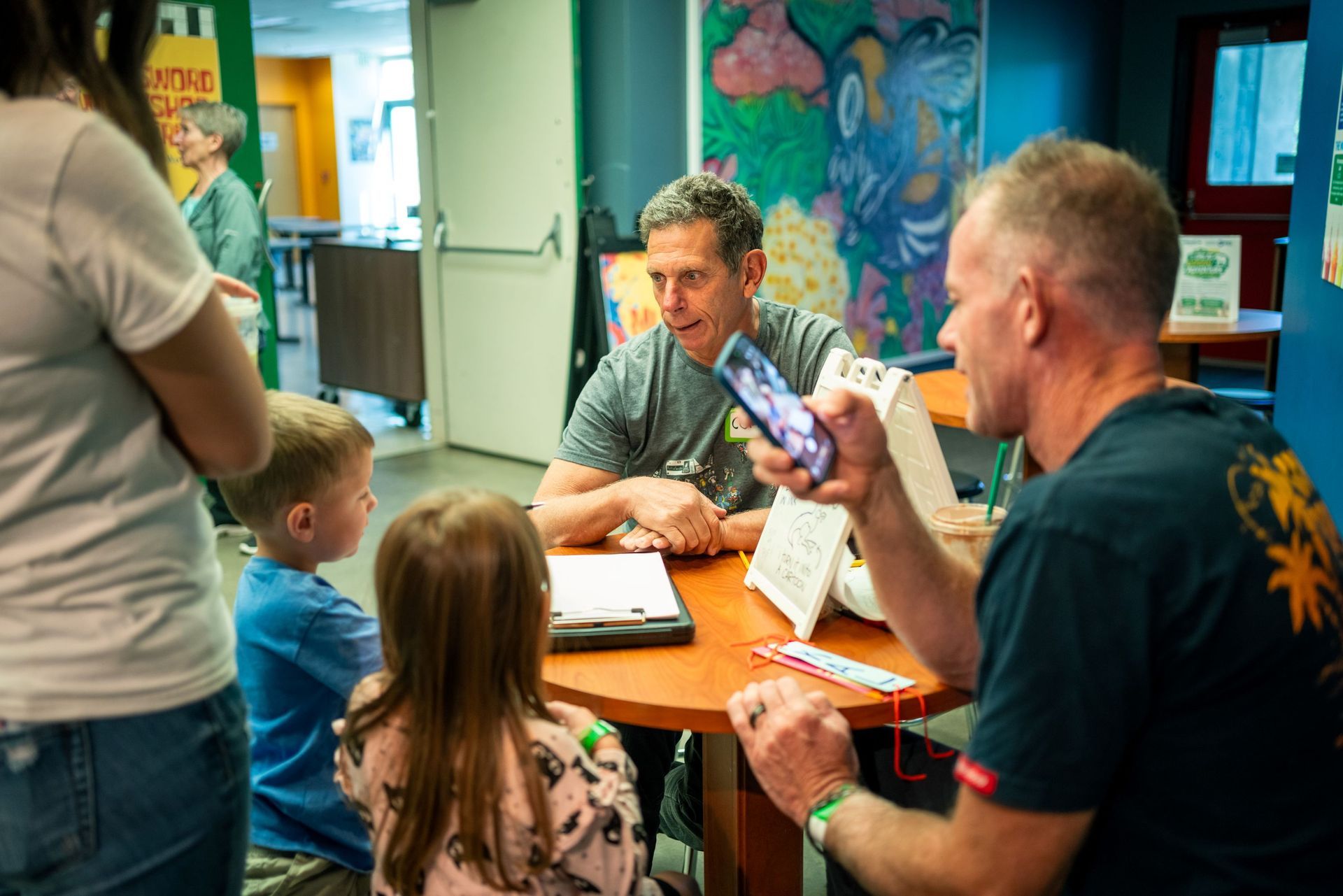 People gathered around a table in a colorful room, looking at a notebook.