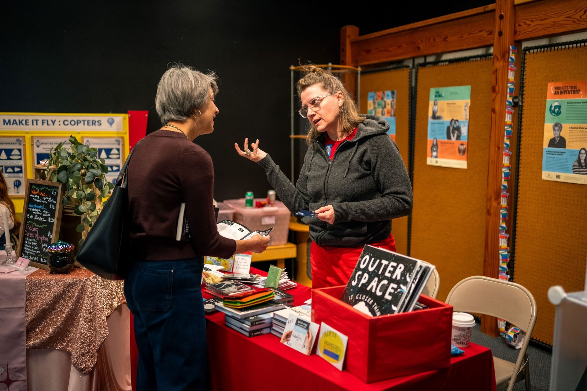 Two people talking at a fair booth with a red table and display signs