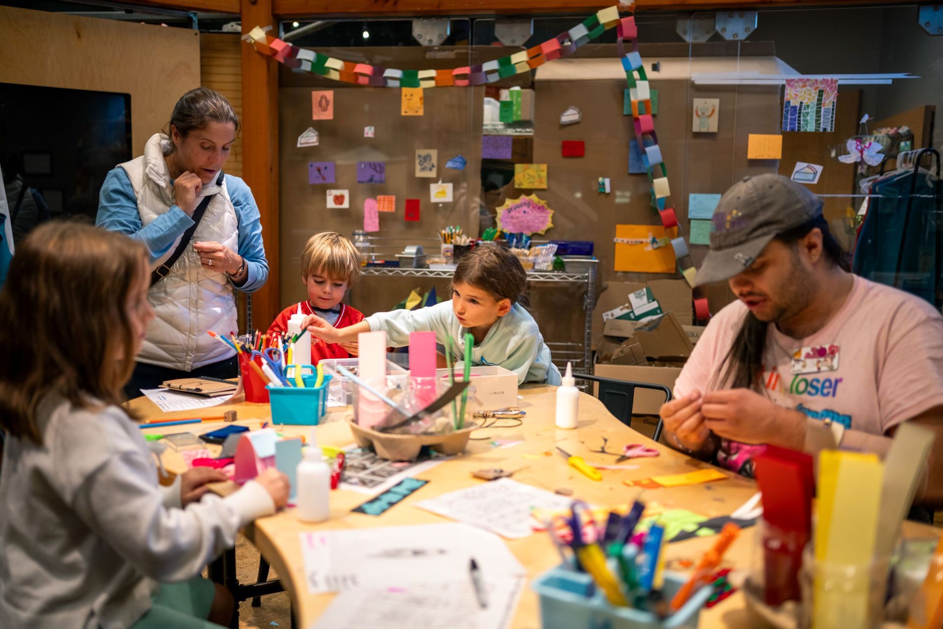 Children and adults crafting at a table in a colorful room decorated with notes and garlands