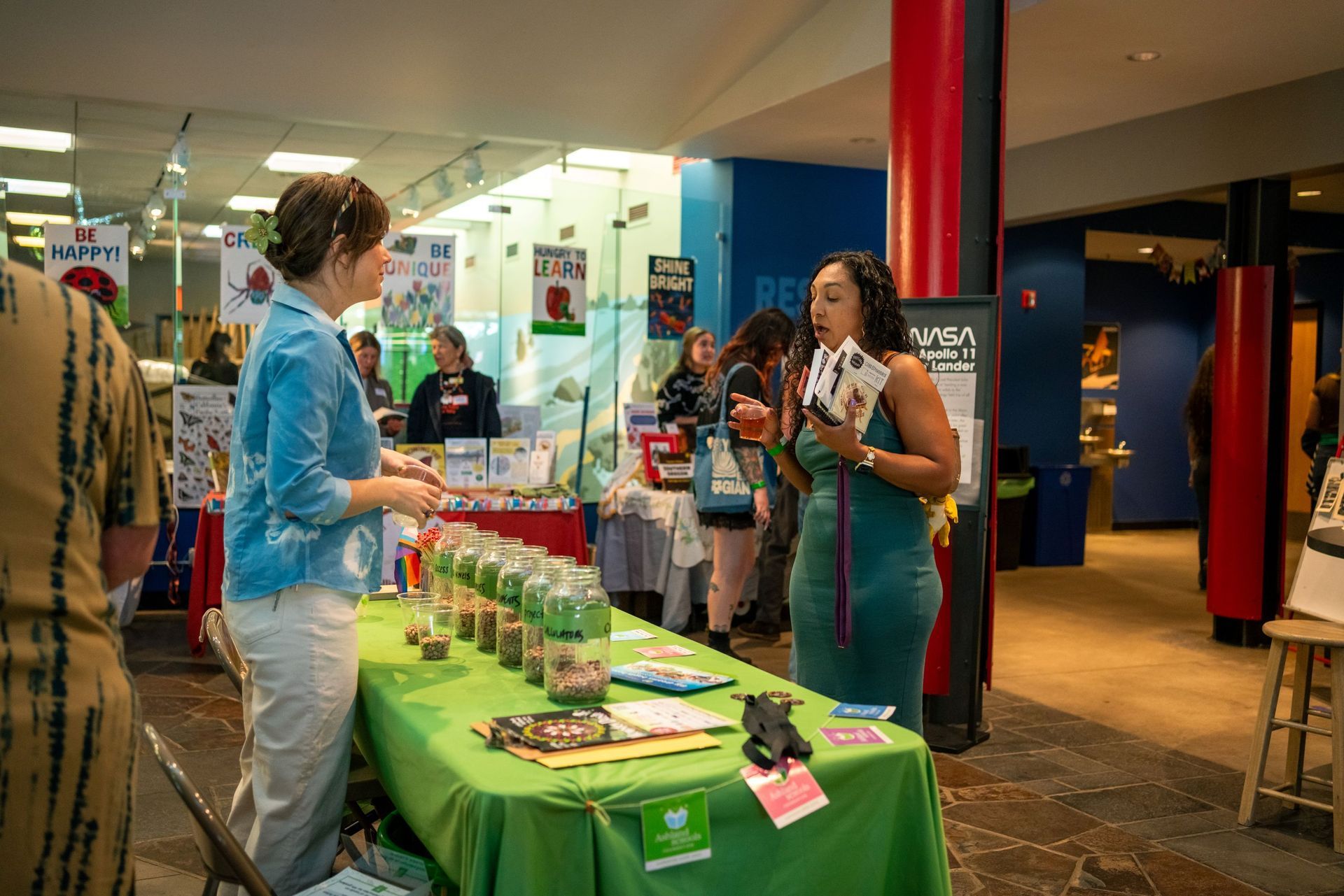 People at a green-covered booth in a hall, with display items on the table