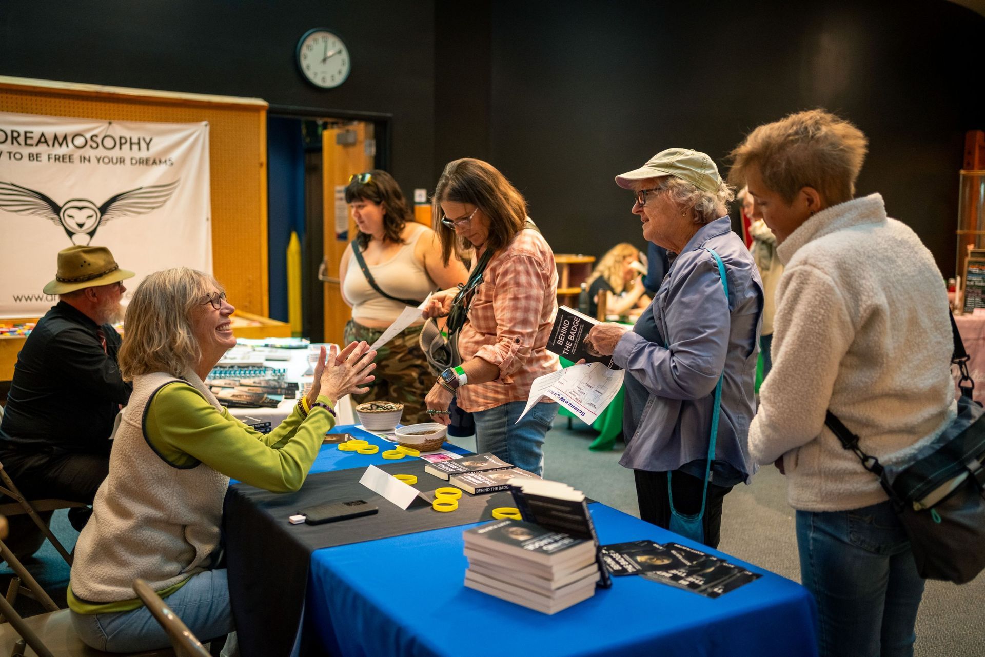 People browsing a vendor table at a booth with books and pamphlets on a blue cloth