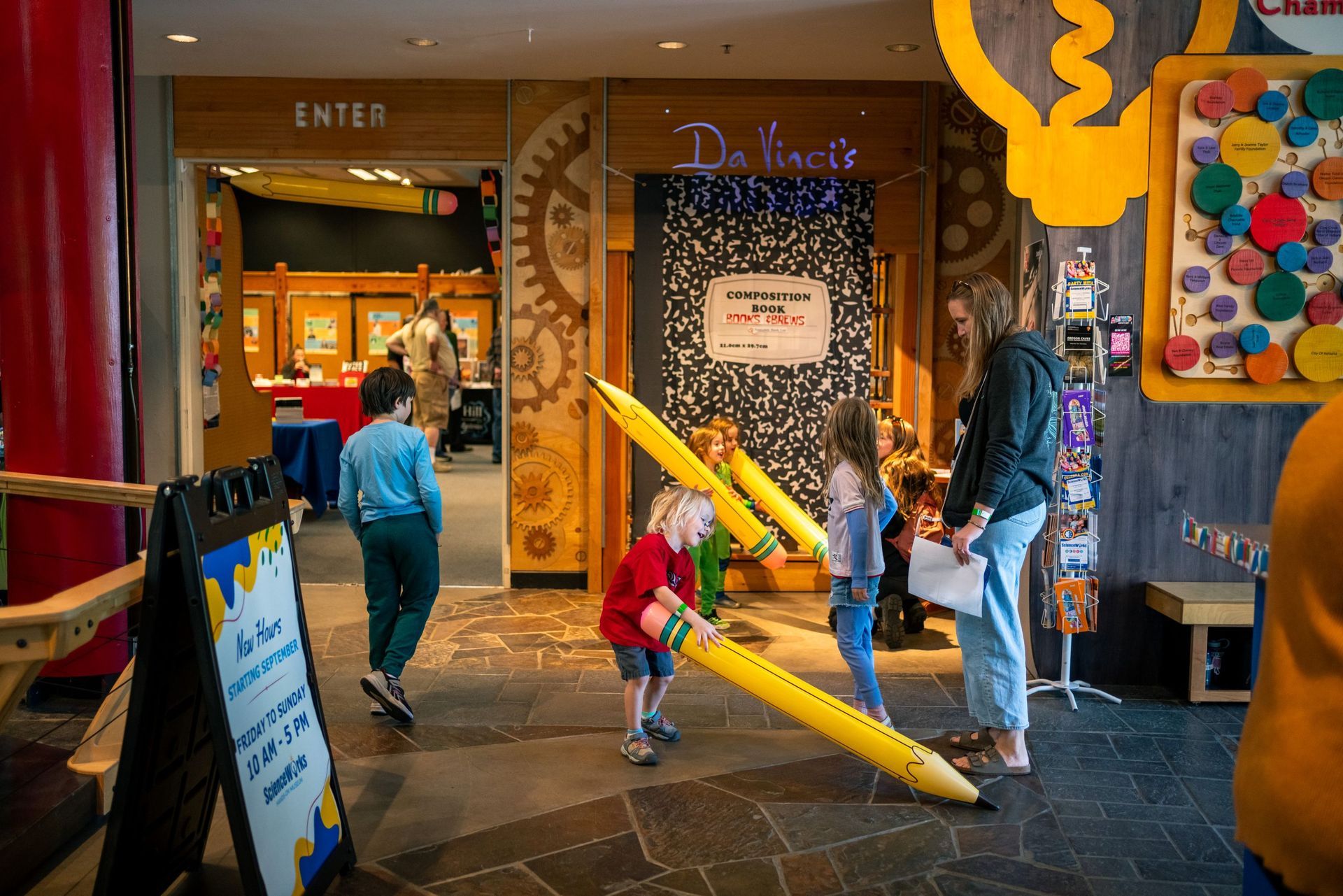 Children playing with giant yellow pencils in a colorful indoor exhibit hall