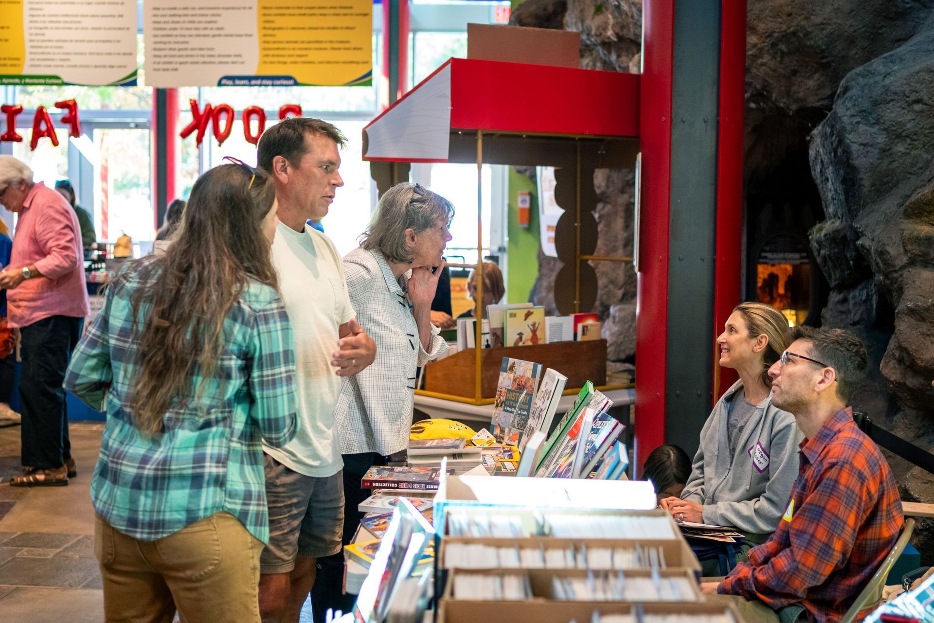 People browsing books at a busy indoor market stall with shelves and tables of magazines or comics