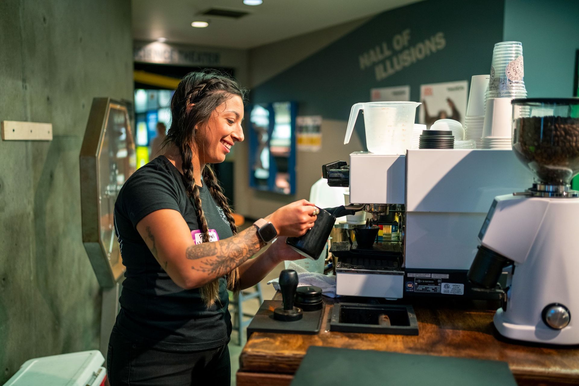 Barista pouring espresso at a coffee booth beside a grinder and stacked cups