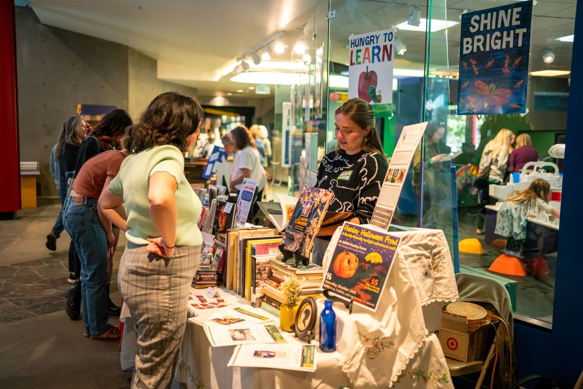 People browsing a vendor booth with books at an indoor market or fair