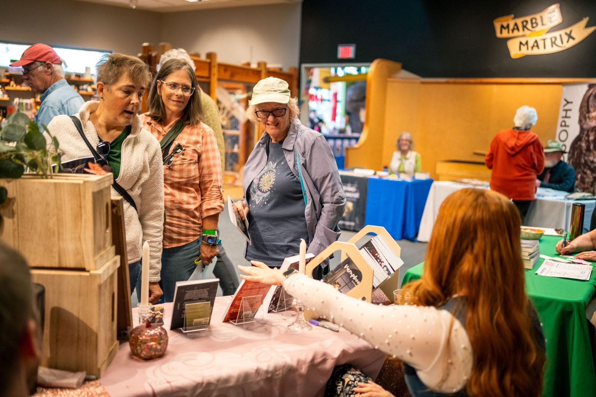 People browsing a fair booth with books, handmade items, and a vendor behind a table
